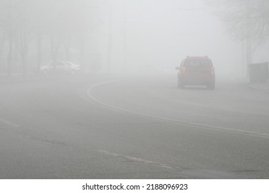 Cars In The Road In City In Fog. Bad Winter Weather And Dangerous Automobile Traffic On The Road. Light Vehicles In Foggy Day. Outdoors