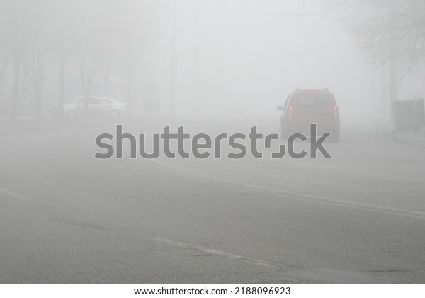 Cars in the road in city in fog. Bad winter\
weather and dangerous automobile traffic on the road. Light\
vehicles in foggy day.\
Outdoors