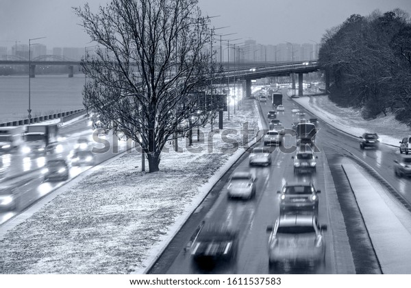 cars rush along the highway in snowy cloudy\
weather with intentional motion\
blur