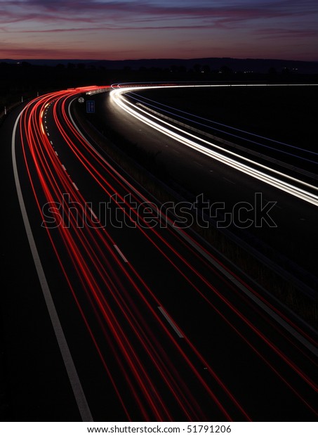 Cars in a rush moving fast on a highway (speedway)\
at dusk