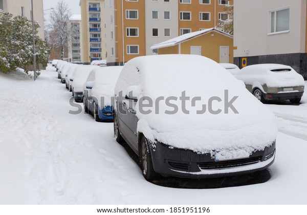 Cars stands on a\
snow-covered road in a wintertime cloudy day. Snowfall in the city,\
cars under the snow.