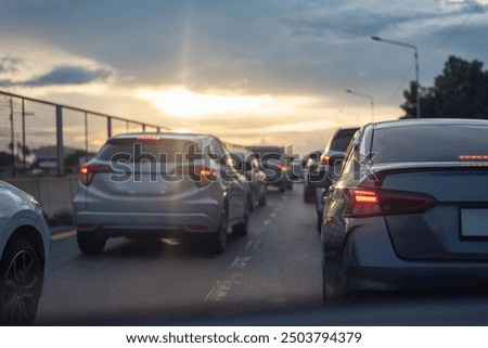 Cars stuck in traffic on a city highway during sunset, with brake lights glowing under a cloudy sky, creating a moody atmosphere.