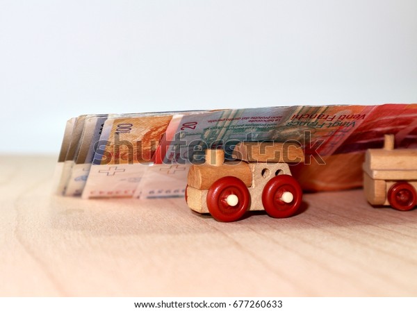 Cars toy\
under pile of money currency on wood\
table\
