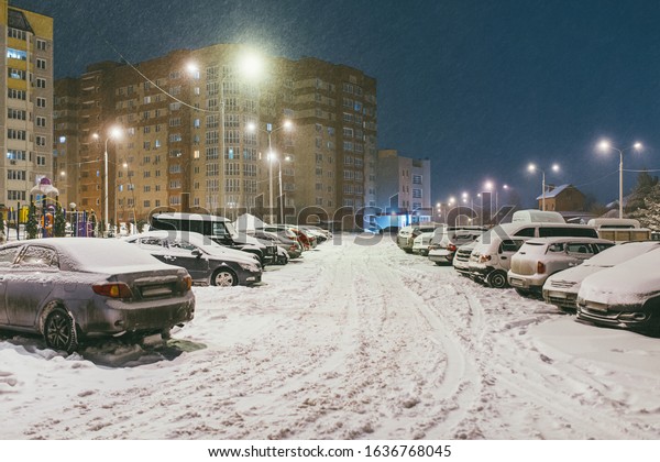 cars in the yard are completely covered\
with snow. In the background is Playground and residential\
buildings with glowing Windows. Quiet winter\
evening