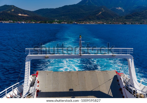Cart\
Ferry sailing away from green island.\
Vehicle ferryboat across\
Aegean Sea at Thassos Greek island on a sunny\
day.