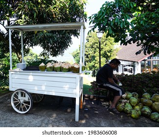 Cart and merchant of Green coconut palm, the seller is peeling the skin to serve the coconut palm water and fruit to the customer. Sentul, Bogor, Indonesia. May, 2021.