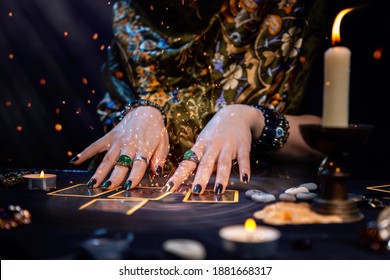 Cartomancy. A fortune teller reads Tarot cards. On the table are candles and fortune-telling objects and sparks. Hands close up. The concept of divination, astrology and esotericism - Shutterstock ID 1881668317