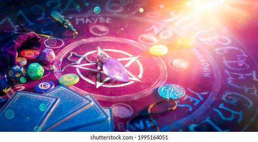 Cartomancy And Tarot - Pendulum On Altar With Defocused Cards And Chakra Stones