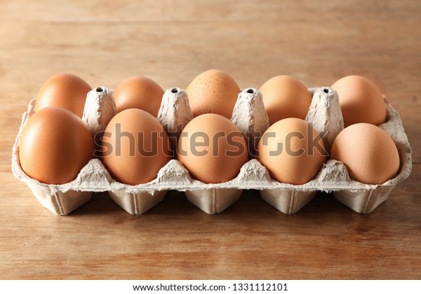 Carton box with\
raw chicken eggs on wooden\
table