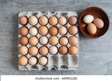 Carton of brown eggs with three selected in a wooden bowl