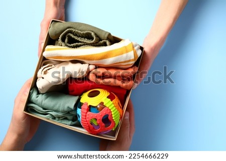 Carton donation box with baby clothes and toy on a color background. Charity concept.