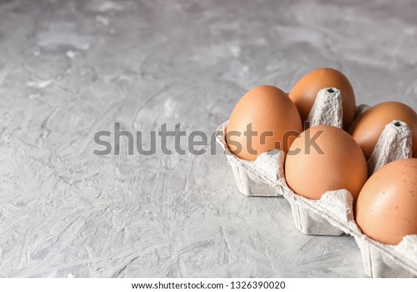Carton pack with\
raw chicken eggs on grey\
table