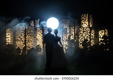 Cartoon Style City Buildings. Realistic City Building Miniatures With Lights. Background. Romantic Couple Silhouettes Standing In From Of Nigth City In Selective Focus