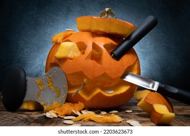 Carved Halloween pumpkin, Jack Lantern with carving tools. Spooky laughing, scary head. Jack-o'-lantern face cut out with spoon gutter, saw blade carvers. Seeds and pieces scattered around.