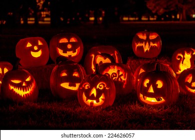 Carved Halloween pumpkins lit with candles sitting on fallen leaves and hay bales