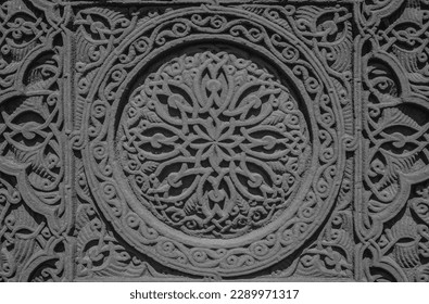 Carved round ornament with intertwining strips forming a pattern placed in a round frame on a red volcanic stone. Traditional tufa stone carving ornament on a wall of Armenian Orthodox Church.