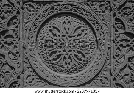 Carved round ornament with intertwining strips forming a pattern placed in a round frame on a red volcanic stone. Traditional tufa stone carving ornament on a wall of Armenian Orthodox Church.