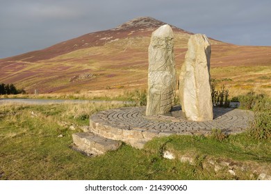 Carved standing stones on a plinth with the heather flanks of Yr Eifl in the distance, Lleyn Peninsular, Gwynedd, Wales, UK.