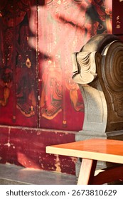 Carved stone column base with cloud scroll ornaments beside a weathered red temple wall adorned with deity paintings. Showcasing ancient craftsmanship with a wooden bench detail.