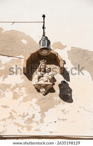 Carved stone virgin on chipped facade with vintage lantern in Denia city, Alicante, Spain