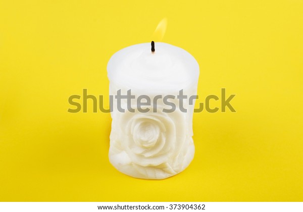 Carved\
white candle on yellow background. Souvenir gift candle in the\
shape of rose. Candle lit. St. valentine\'s day.\
