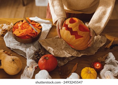 Carving halloween pumpkin. Woman holding pumpkin and knife on table with ghosts and spiders. Carve a jack o lantern, halloween preparation. Making halloween decorations - Powered by Shutterstock