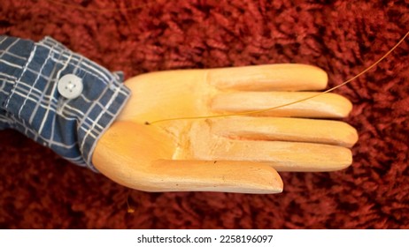 carving hand and arm of a wooden puppet or handmade marionette, painted and dressed in cloth of a shirt isolated on a red carpet in the background - Shutterstock ID 2258196097