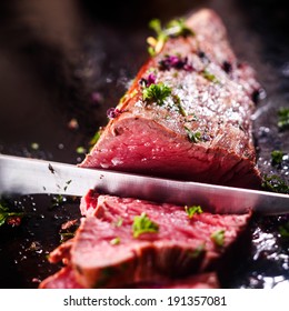 Carving A Portion Of Delicious Rare Roast Beef Sirloin Of Fillet Seasoned With Fresh Herbs With A Large Steel Carving Knife