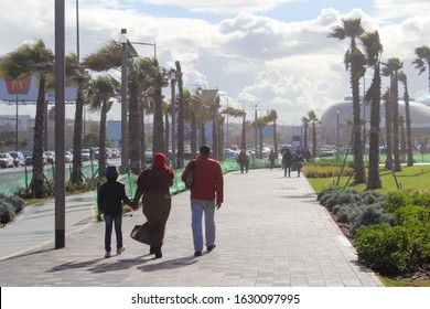 Casablanca, Morocco / Saturday January 25 2020 - A moroccan family happily walking down a palm tree lined sidewalk together holding hands towards the Morocco Mall on a cloudy day in Casablanca.