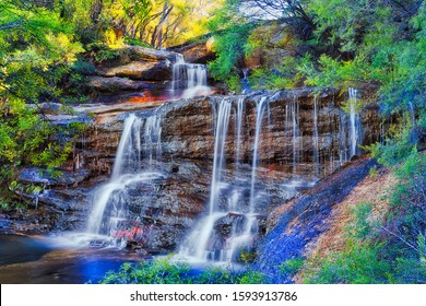 Cascade of waterfalls in Australian Blue Mountains cutting through sandstone rocks in evergreen gum tree forest on sunny winter morning.