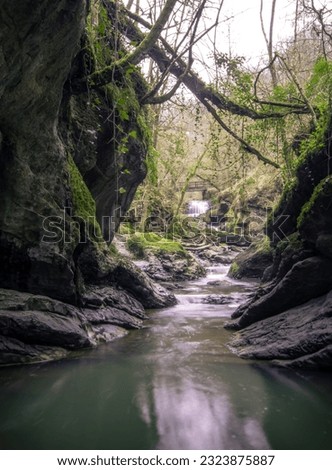 Cascades flowing through open cave system, waterfall in the distance, moody aesthetic, high quality imaging, vines hanging from the rocks, long exposure