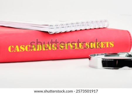 Cascading style sheets are displayed on a vibrant red binder alongside a silver clip, highlighting the importance of organized resources for effective web design and development.