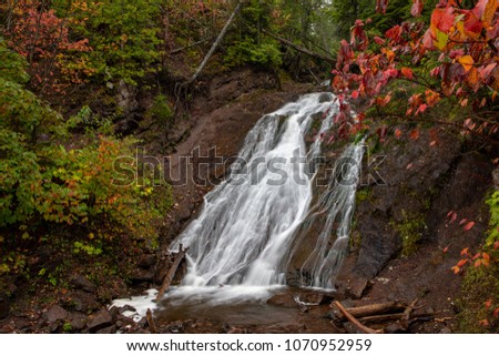 Cascading water flows rapidly over Jacobs Falls near Eagle River Michigan. Autumn colors and rock walls in the background. Near the popular Jam Pot