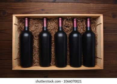 Case of Red Wine: Top view of a wood case of red wine bottles on a dark wood table, the case is filled with packing straw.
