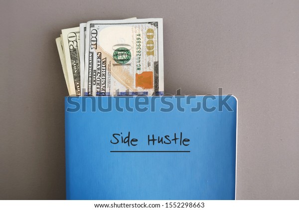 Cash dollar money in a\
blue notebook with text written on cover SIDE HUSTLE, on grey\
background, concept of making more money from side job with writing\
or freelance job