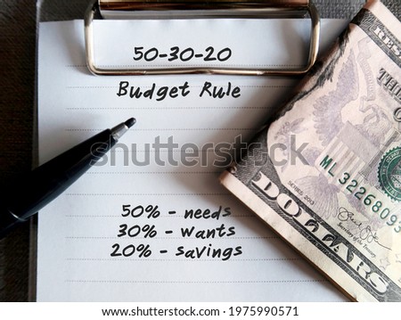 Cash dollars money ,pen and notebook with text written - 50 30 20 RULE , 50% NEEDS 30% WANTS 20% SAVINGS - Rule of Thumb for allocating budget to reach financial goals