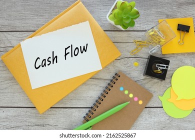 Cash Flow. Torn Page From A Notebook With Text. Yellow Notepad On A Wooden Background. Notepad Near Plant In A Pot Of Stickers