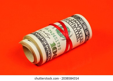 Cash hundred-dollar bills in a roll, tied with a red ribbon, on a red background. Money to pay for purchases in the store of goods and services.