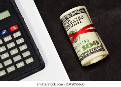 Cash hundred-dollar bills in a roll, tied with a red ribbon. Money to pay for purchases in the store of goods and services. And a calculator for planning and monitoring financial transactions.