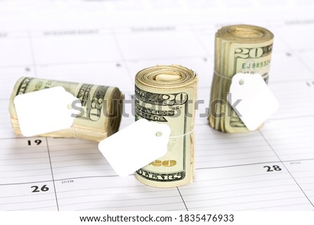 Cash money rolls on a desk calendar with blank tags for copy