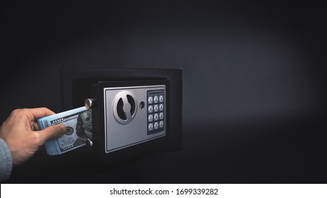 Cash Money Safe Deposit. Symbol Of Money Safety. The Man Puts A Wad Of Dollars In Small Residential Vault. Toned Soft Focus Picture. Copy Space