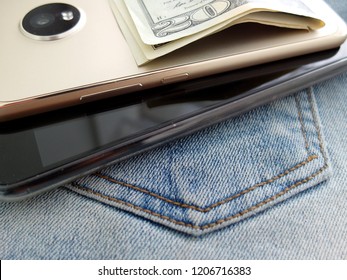 Cash money and smart phone on blue jeans background implying a young small business owner who start online business or e-commerce to make money.