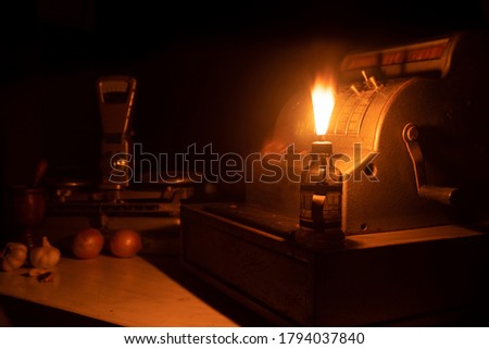 
cash register, scale, spices and old money lit by the flame of an old lamp on wooden table, "Low Key" image selective focus.
