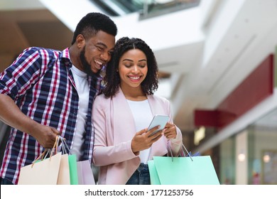 Cashback Concept. Happy Black Couple With Smartphone Checking Bank Account After Successful Shopping In Mall, Free Space