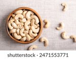 Cashew nuts, raw cashews in a wooden bowl on linen fabric. Seeds of shelled fruits of cashew tree Anacardium occidentale. Used as snack nuts, and in recipes, or processed into cashew butter or cheese.