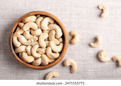 Cashew nuts, raw cashews in a wooden bowl on linen fabric. Seeds of shelled fruits of cashew tree Anacardium occidentale. Used as snack nuts, and in recipes, or processed into cashew butter or cheese.