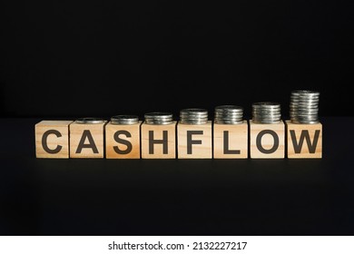 cashflow text written on wooden block with stacked coins on black background, business concept