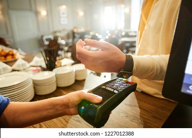 Cashier holding payment machine while one of clients with smartwatch keeping his wrist over it