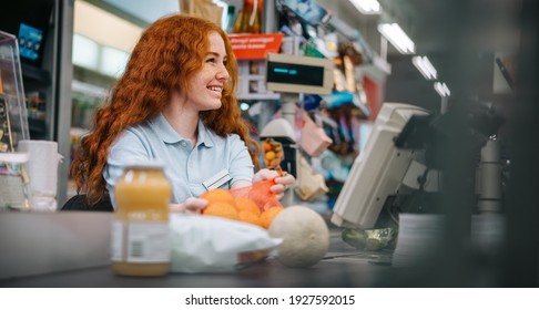 Cashier Packing Food Products For Customer At Checkout Counter. Young Worker Working At Supermarket Checkout Counter.