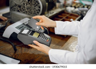 Cashless payment at pharmacy. Cropped close up shot of hands of female unrecognizable pharmacist in lab coat, working at pharmacy and swiping credit card through the terminal